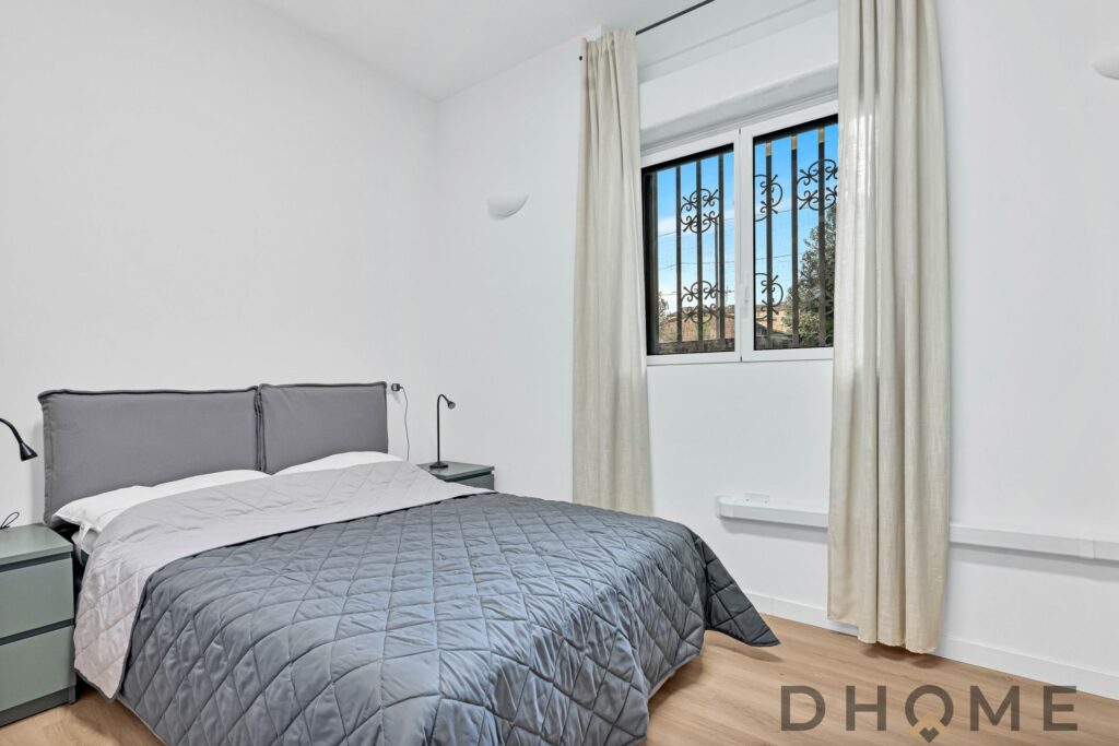 Elegante camera da letto con parete bianca, letto matrimoniale e finestra con inferriate.