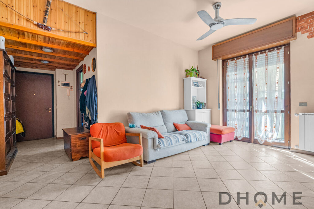 Soggiorno luminoso con divano, poltrona arancione e accessori decorativi moderni.