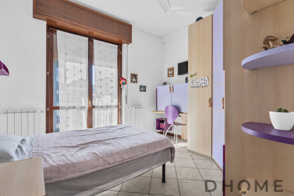 Camera da letto moderna con grandi finestre, arredi color lilla e spazio di lavoro dedicato.