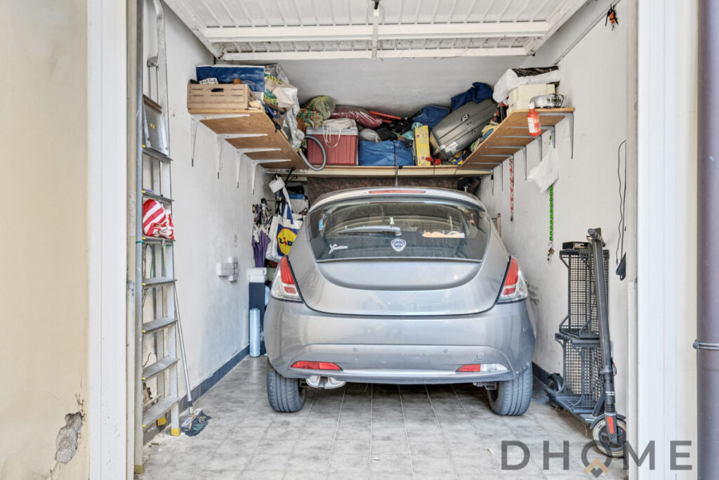 Auto parcheggiata in garage con scaffali e varie attrezzature domestiche.