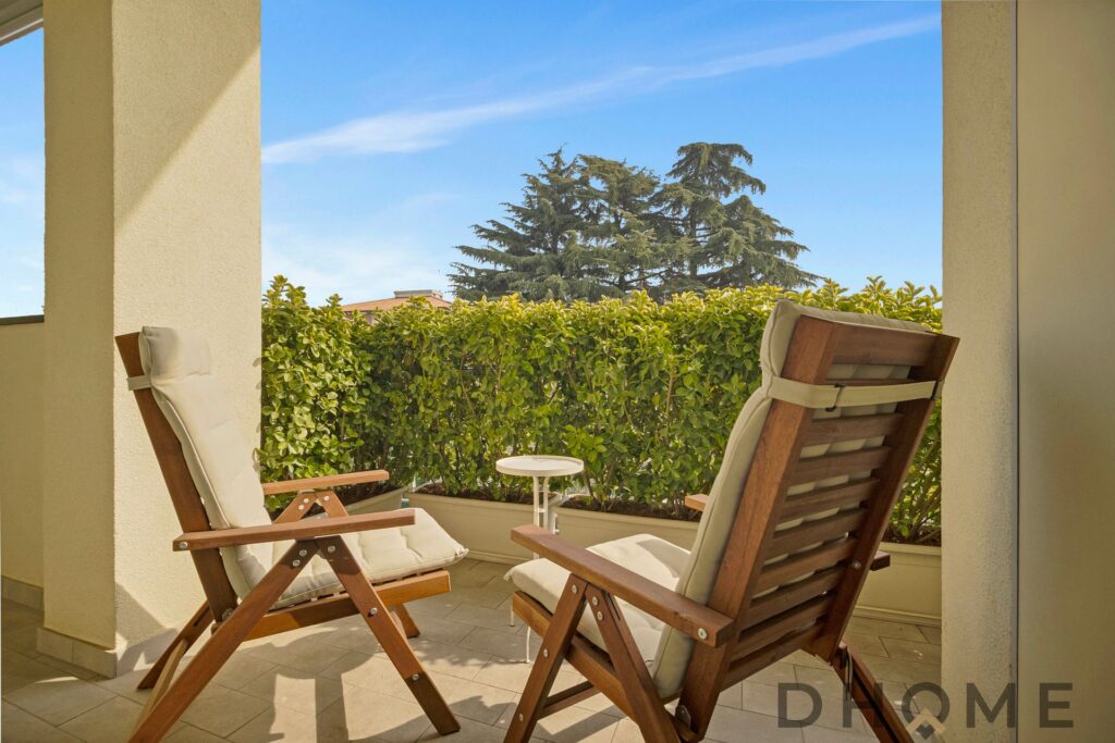 Balcone ampio con sedie in legno e vista su giardino e cielo azzurro.
