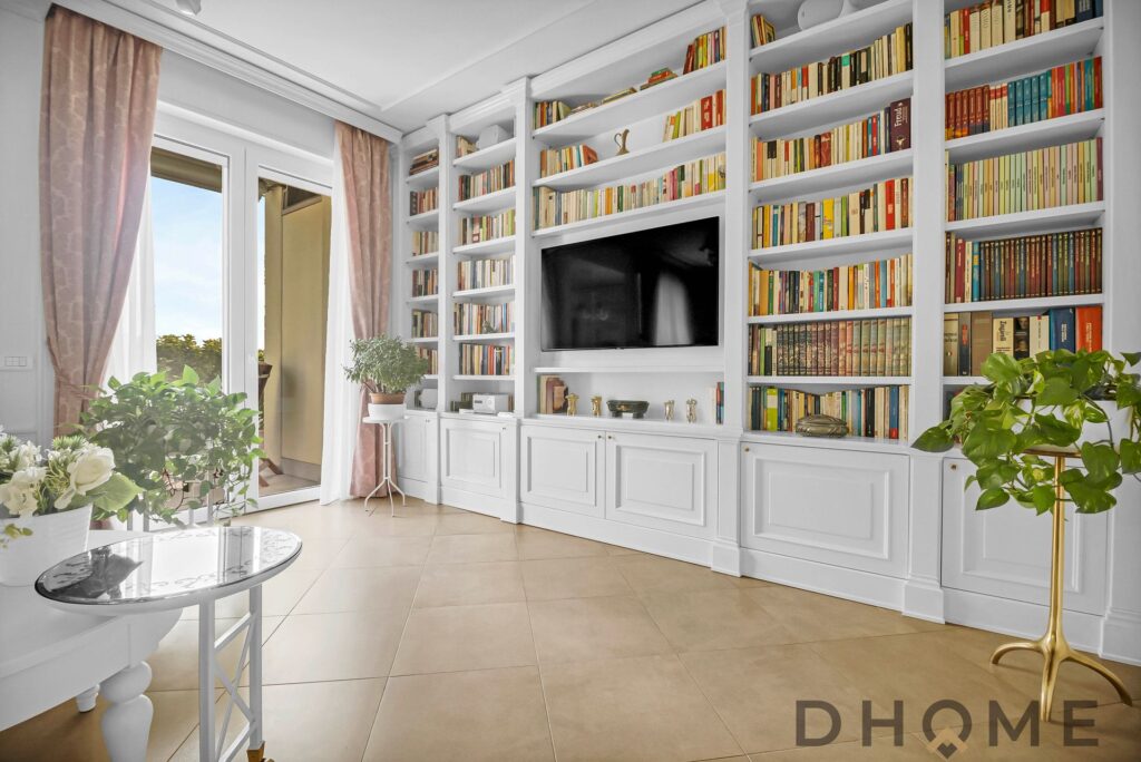 Soggiorno con libreria a parete, TV e ampie finestre luminose.