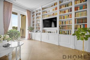 Soggiorno con libreria a parete, TV e ampie finestre luminose.