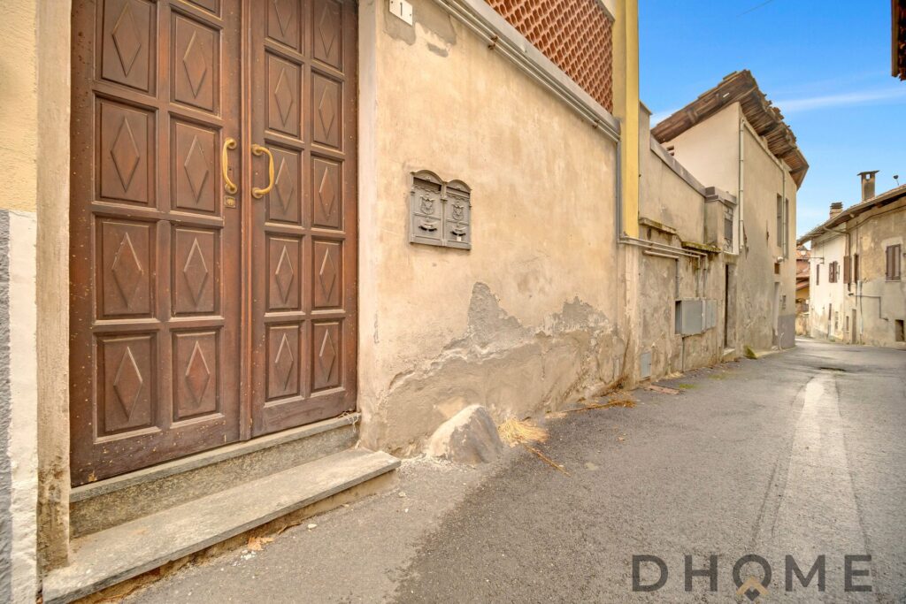 Casa storica con porta in legno e strada di paese in Agliè.