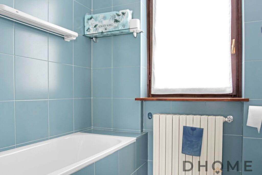 Vasca da bagno moderna in bagno con piastrelle azzurre e finestra naturale.