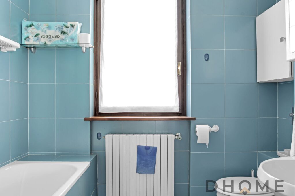 Bagno in appartamento quadrilocale a Primaluna con piastrelle azzurre e finestra luminosa.