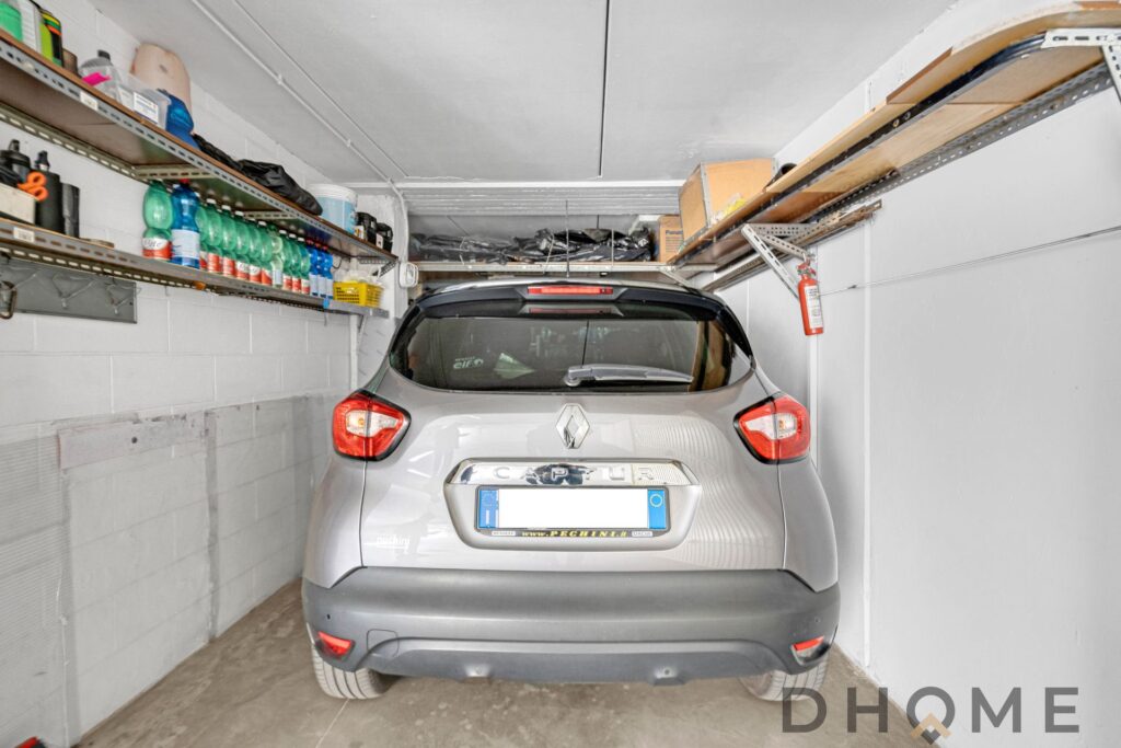 Auto in garage con scaffalature e attrezzi, spazio di parcheggio coperto.