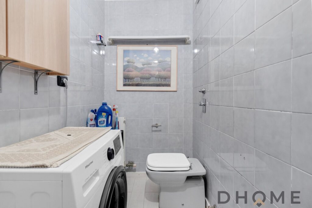 Lavanderia con lavatrice, bagno con WC e balcone in zona residenziale di Milano.