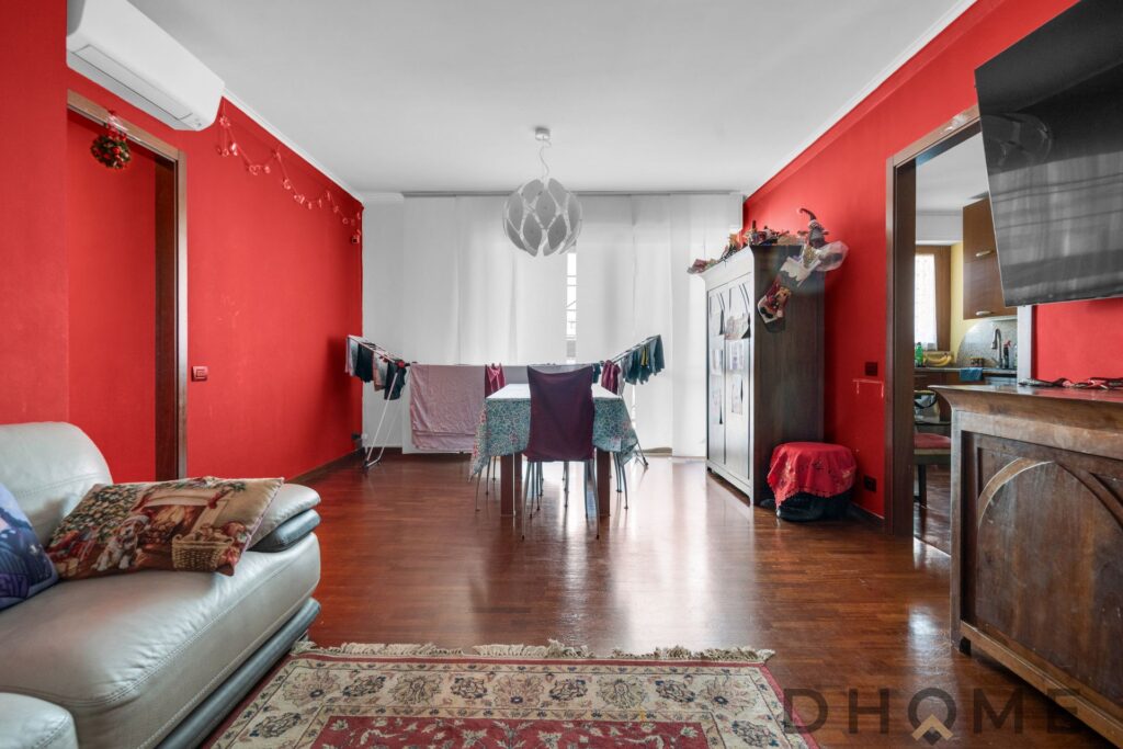 Ampio soggiorno con pareti rosse, balcone e zona pranzo.